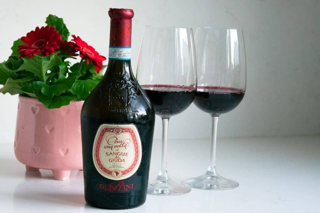 Sangue di Giuda wine and 2 glasses with a pink flower pot in the background