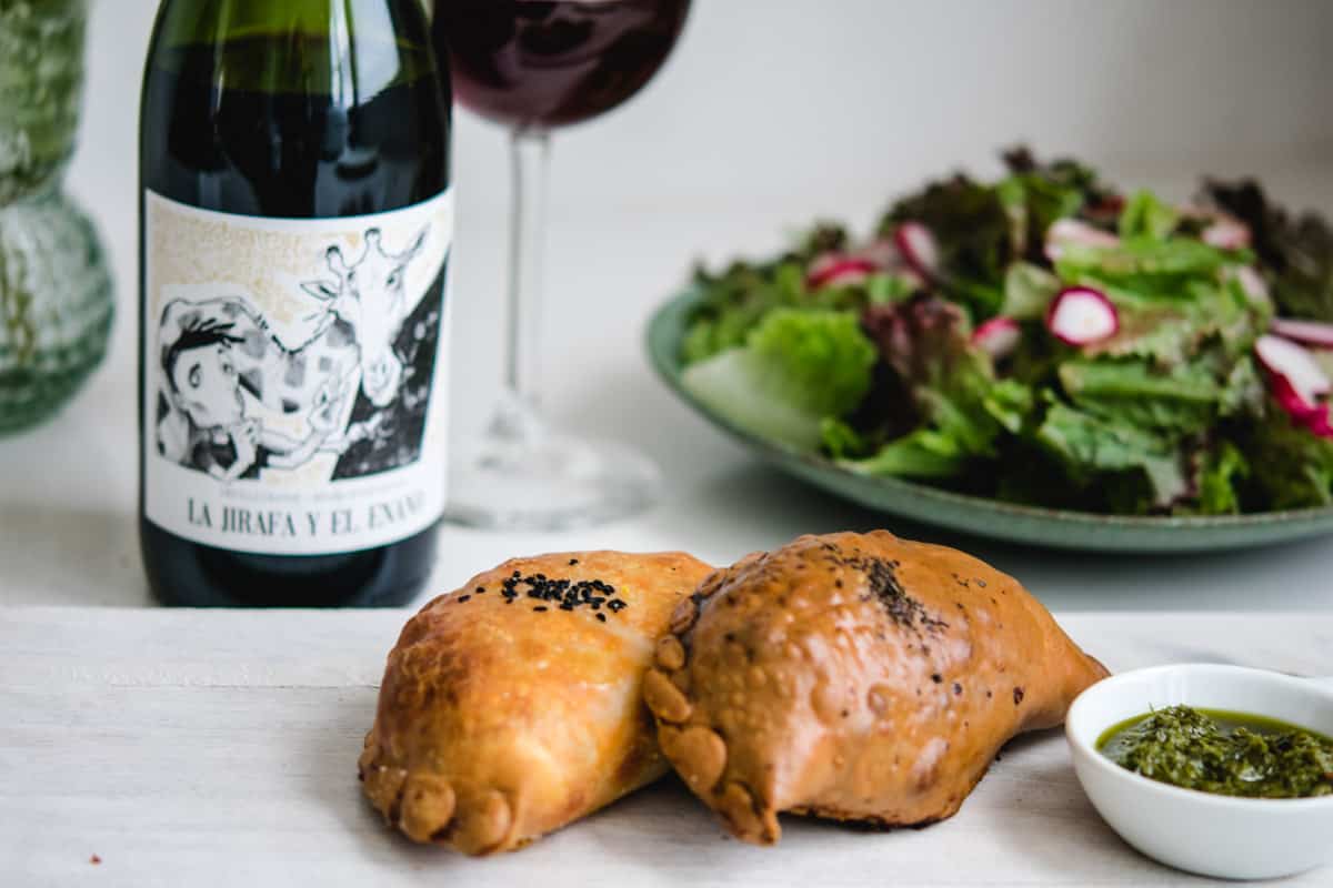 2 empanadas on a white board with chimichurri sauce
