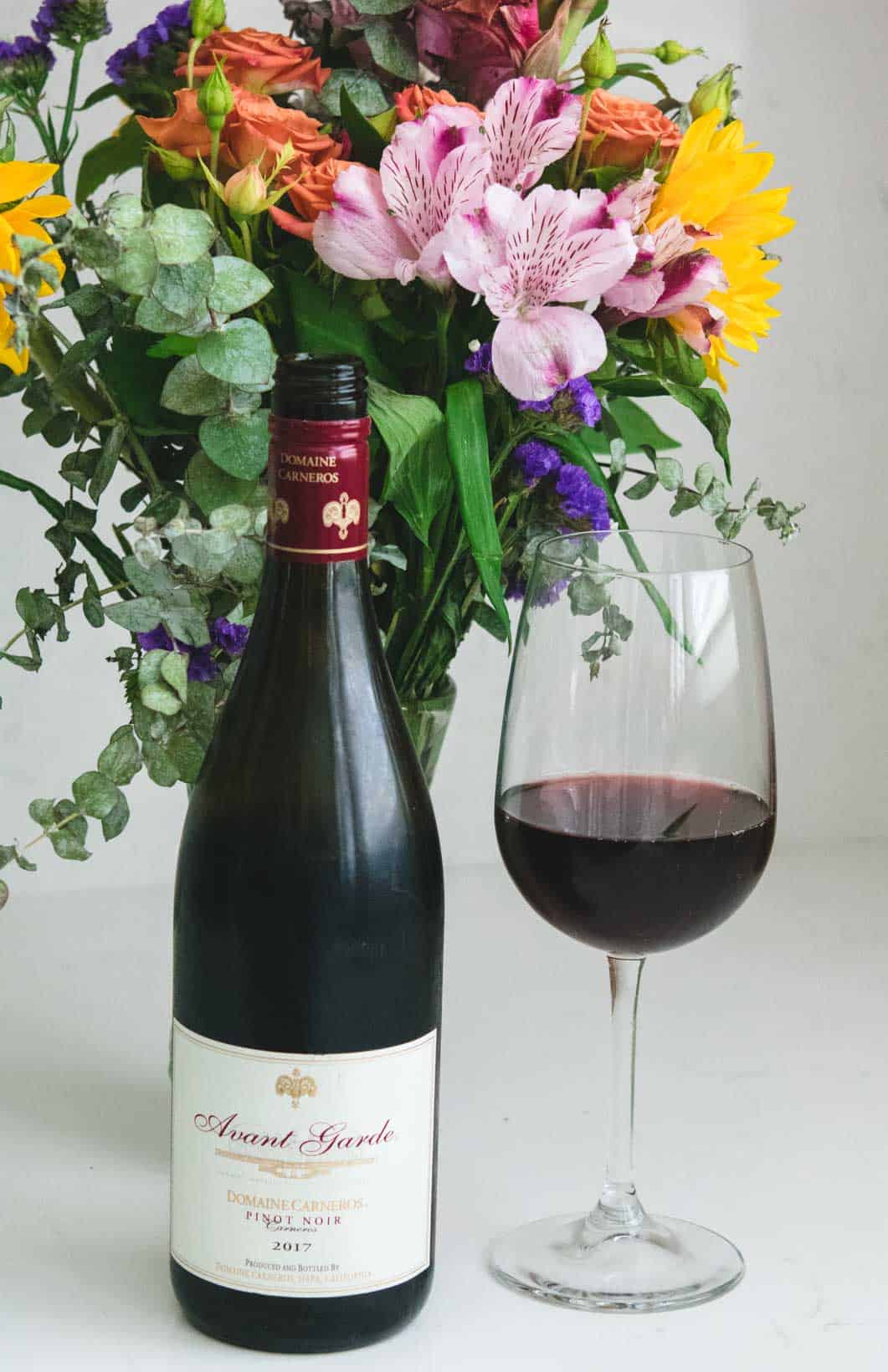 Vertical shot of Domaine Carneros bottle and glass of Pinot Noir with flower bouquet in the background