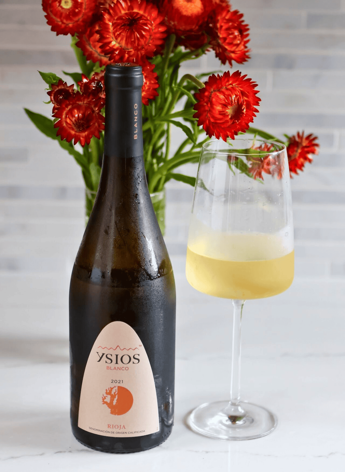 Ysios bottle and glass of white wine with red flowers in the background