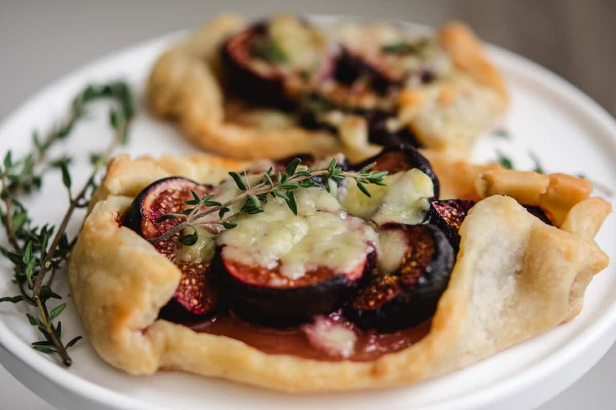 Fig and Blue cheese tarts with fresh thyme springs on a white cake stand.