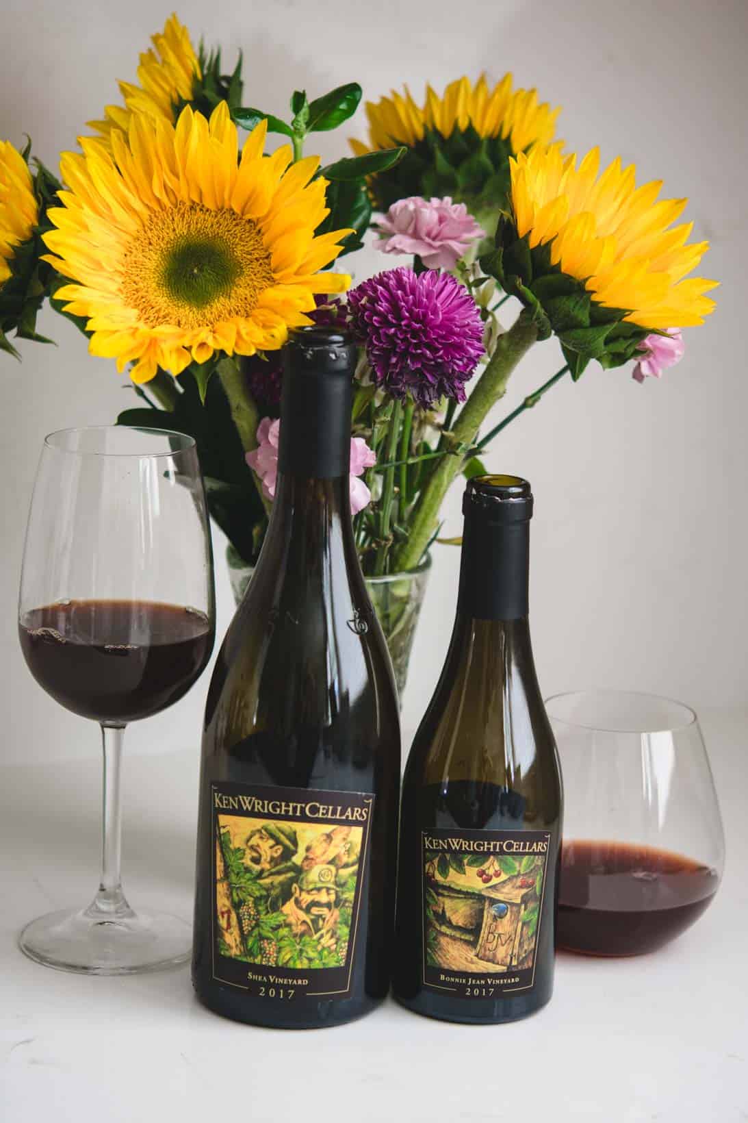 1 bottle and 1 half bottle of Ken Write Pinot Noir wines with sunflowers in the background