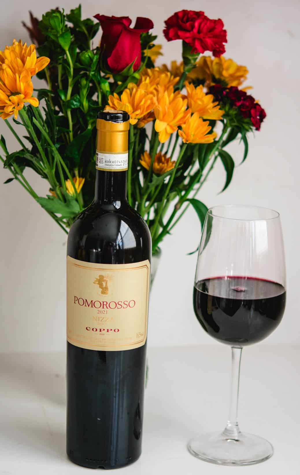 glass and bottle of Pomorosso wine from Coppo with flowers in the background