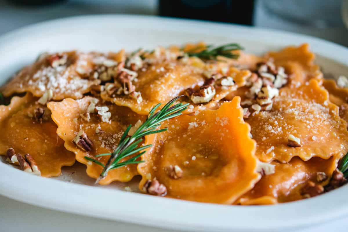 Orange butternut squash ravioli with pecans and rosemary garnish