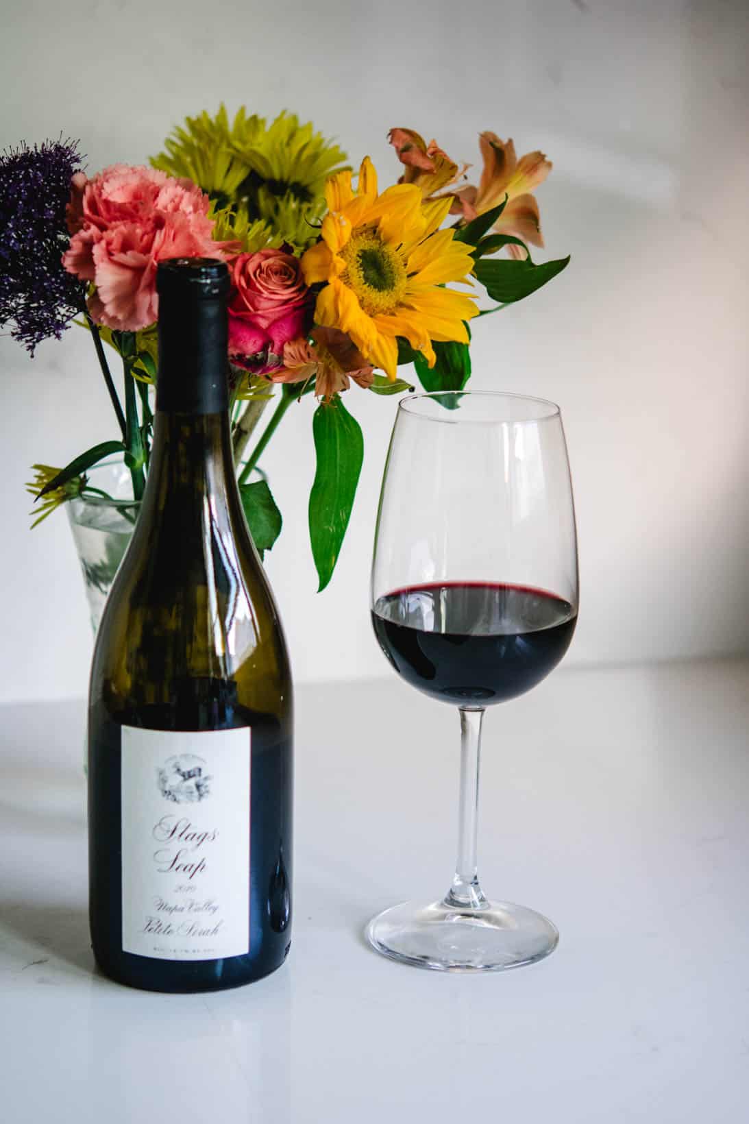 Stags' Leap Petite Sirah wine bottle and glass with flowers in the background