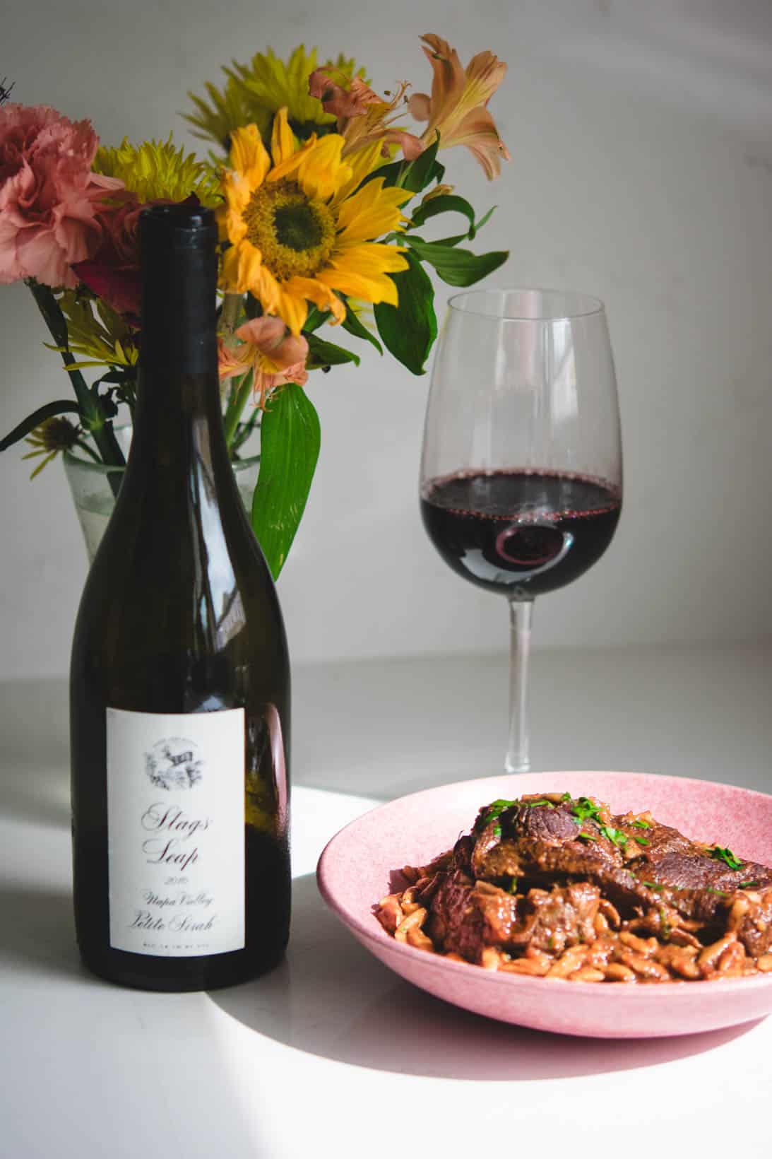 Stags' Leap Petite Sirah wine bottle and glass with flowers in the background and a pink bowl of lamb manastra